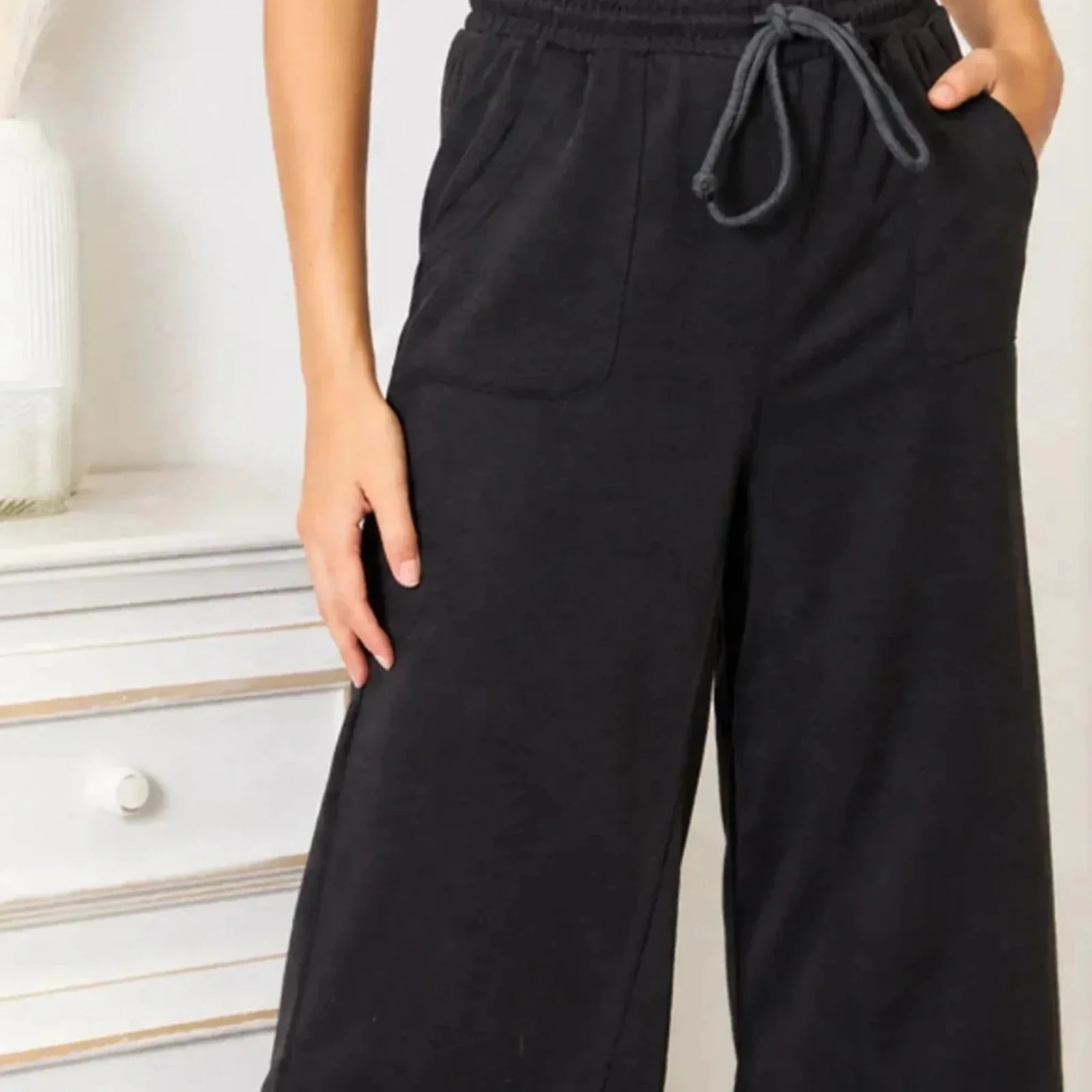 Close-up of black wide leg lounge pants featuring an elastic drawstring waistband and front pockets.
