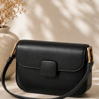 Black faux leather shoulder bag displayed on a neutral background showcasing the structured design, magnetic flap closure and gold hardware.