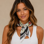 Woman wearing a black floral multi print square scarf tied around the neck with a classic black border and colorful floral pattern.