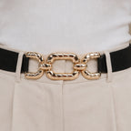 Close-up of a black elastic waist belt featuring a textured gold chain buckle.