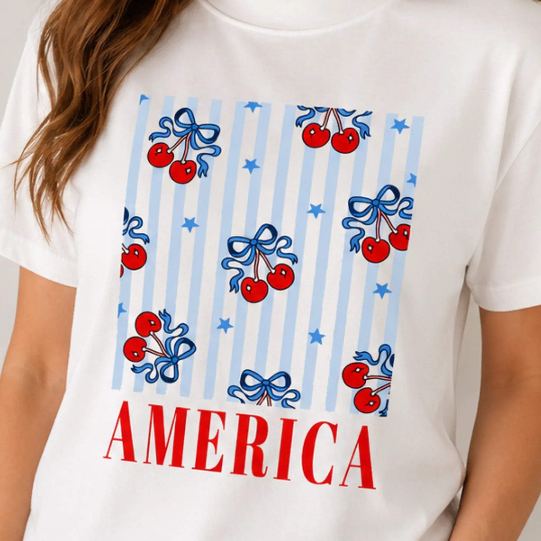 Close-up of the Bow Cherry America Patriotic Graphic Crewneck T-Shirt featuring a patriotic cherry bow graphic and America lettering.