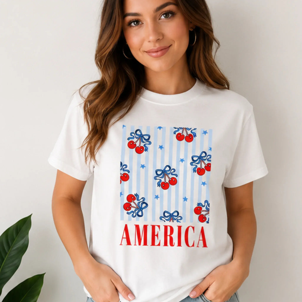 Woman wearing the Bow Cherry America Patriotic Graphic Crewneck T-Shirt in white with cherry bow patriotic print.
