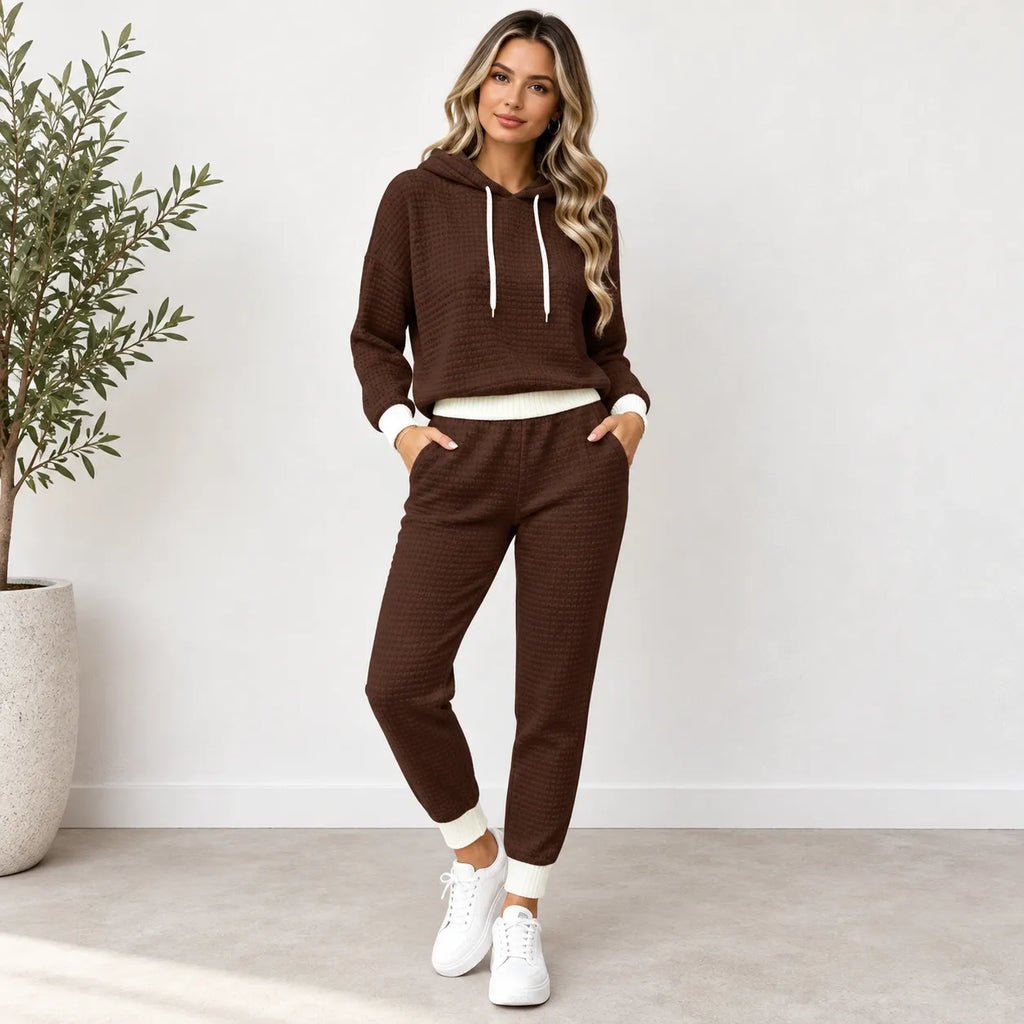 A woman modeling a matching brown waffle-knit lounge set consisting of a pullover hoodie and jogger pants, styled with white sneakers in a bright indoor setting.