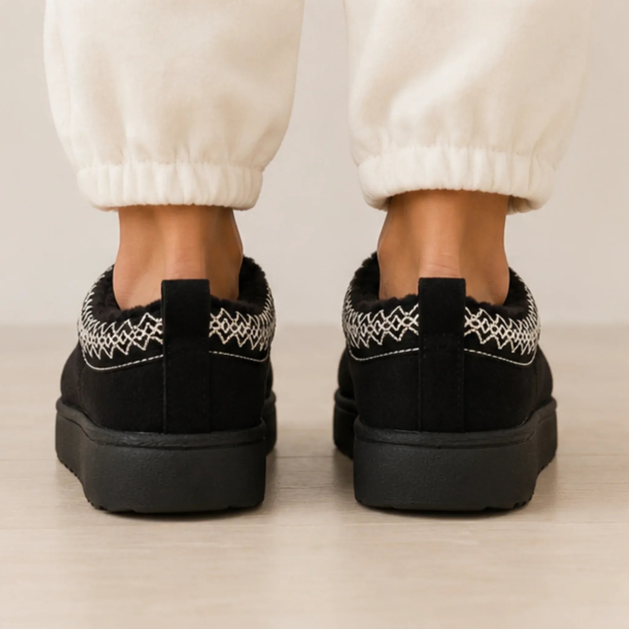 Rear view of black Cozy Fleece-Lined House Slippers showing the pull tab, embroidered collar trim, and durable platform sole.