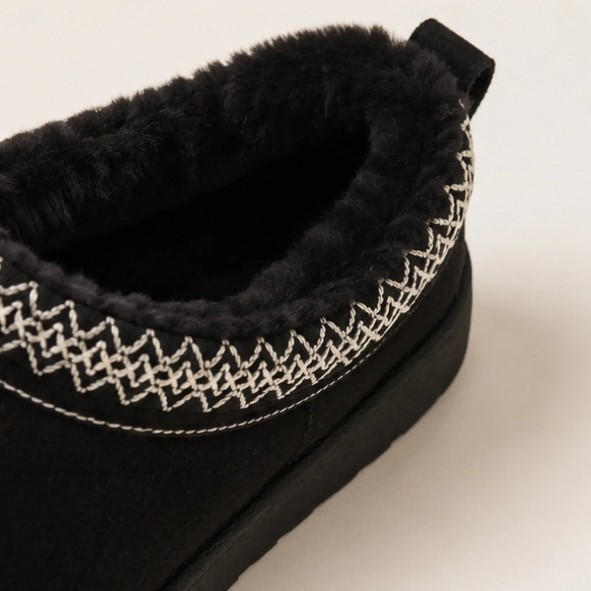 Close-up of black Cozy Fleece-Lined House Slippers highlighting the ultra-soft fleece lining, embroidered collar, and suede-look upper.