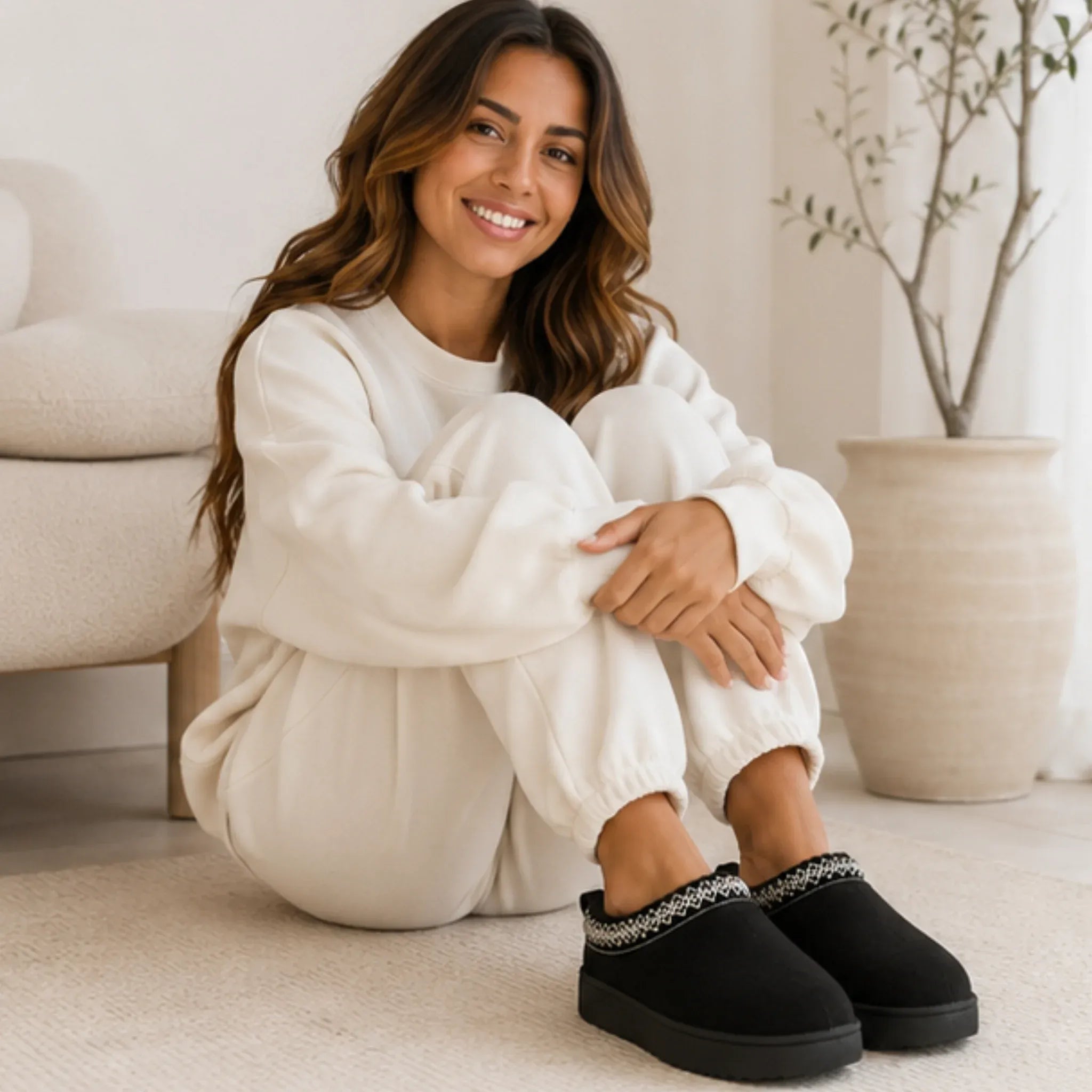 Woman relaxing indoors wearing black Cozy Fleece-Lined House Slippers with a soft suede upper, plush fleece lining, and cushioned platform sole.