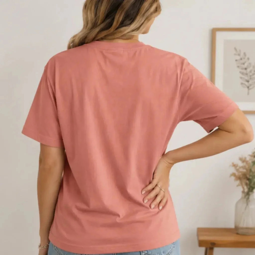 Back view of a woman wearing a dusty rose crew neck graphic t-shirt showcasing the relaxed fit and short sleeve design.