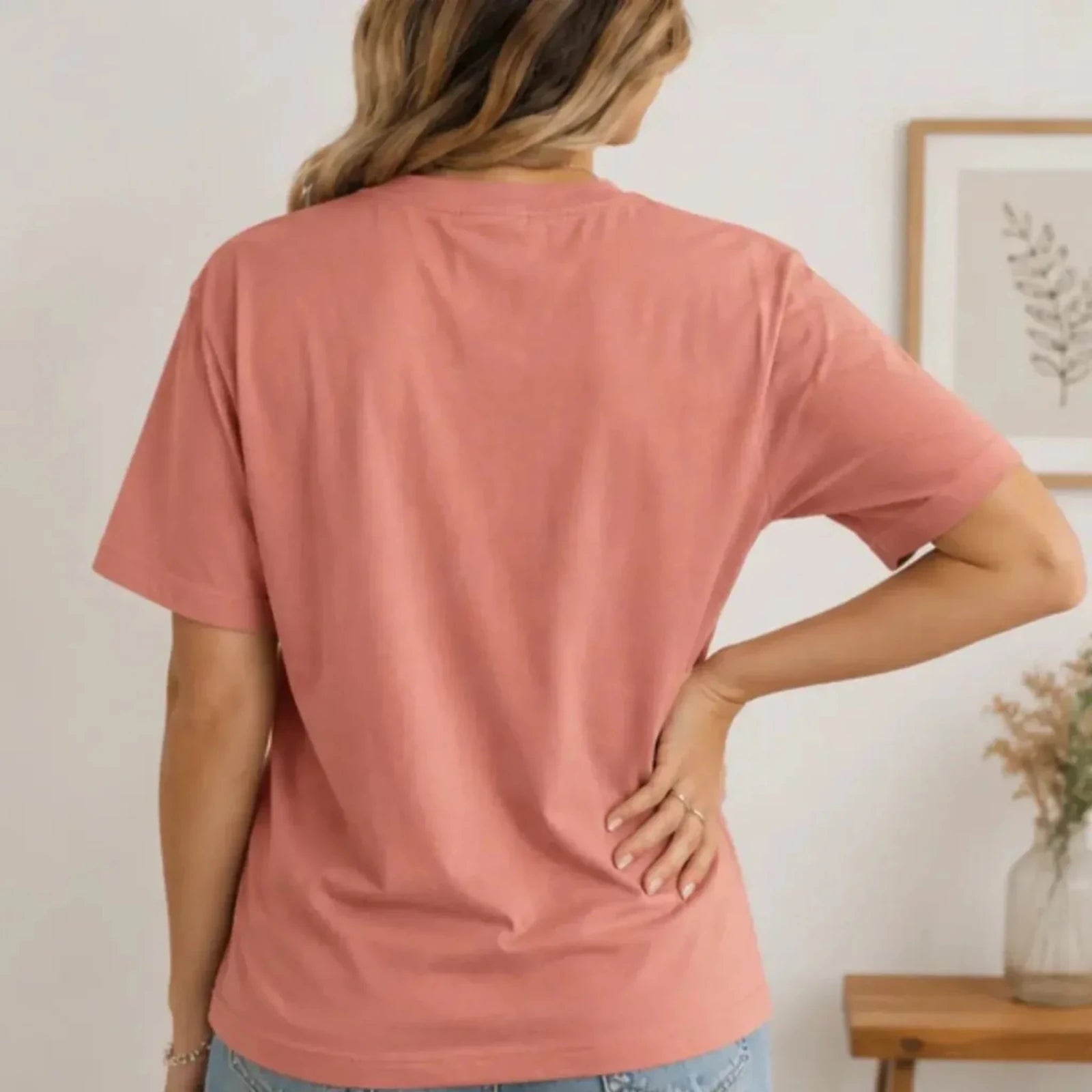 Back view of a woman wearing a dusty rose crew neck graphic t-shirt showcasing the relaxed fit and short sleeve design.