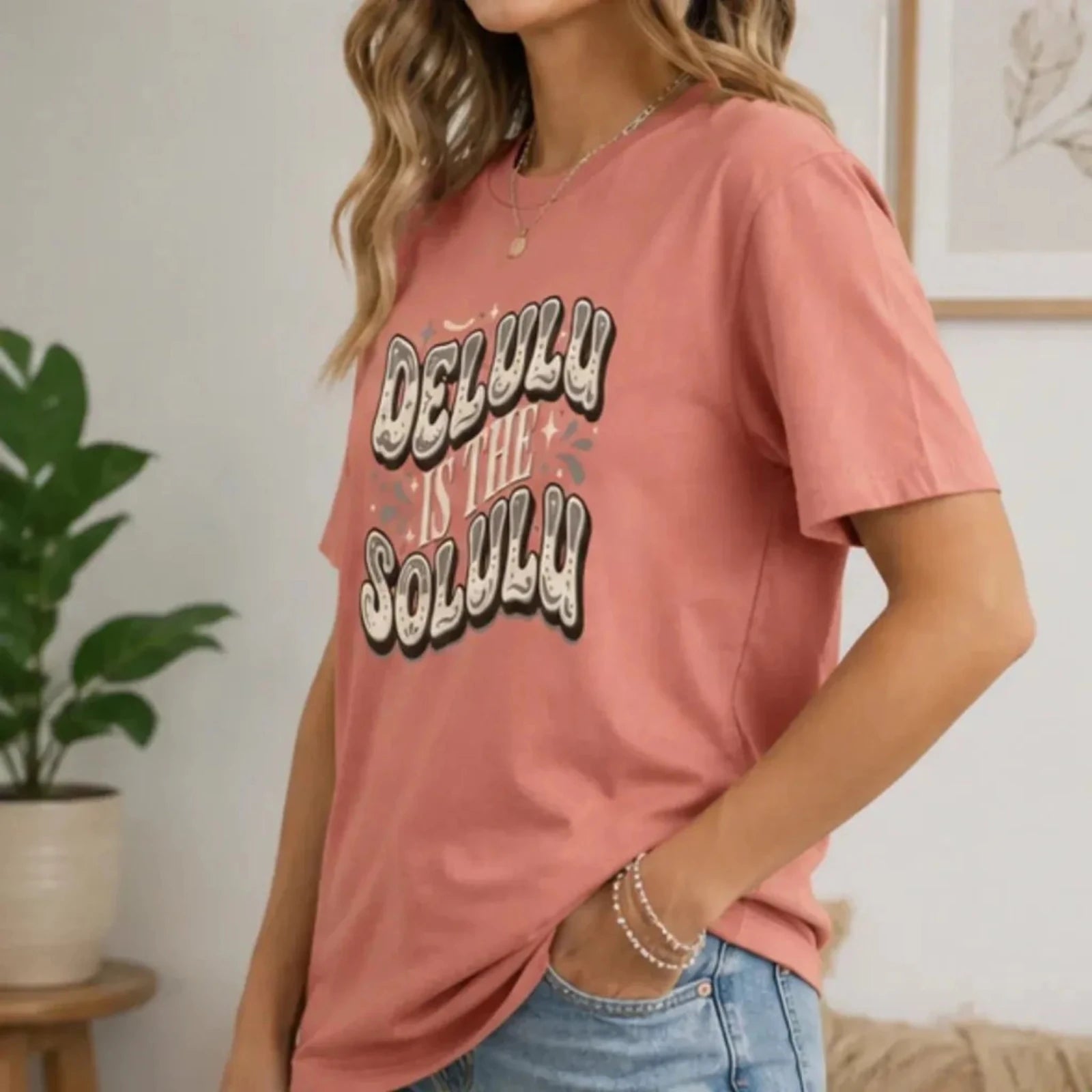 Side view of a woman wearing a dusty rose Delulu Is the Solulu graphic tee styled with light wash jeans for a casual everyday outfit.