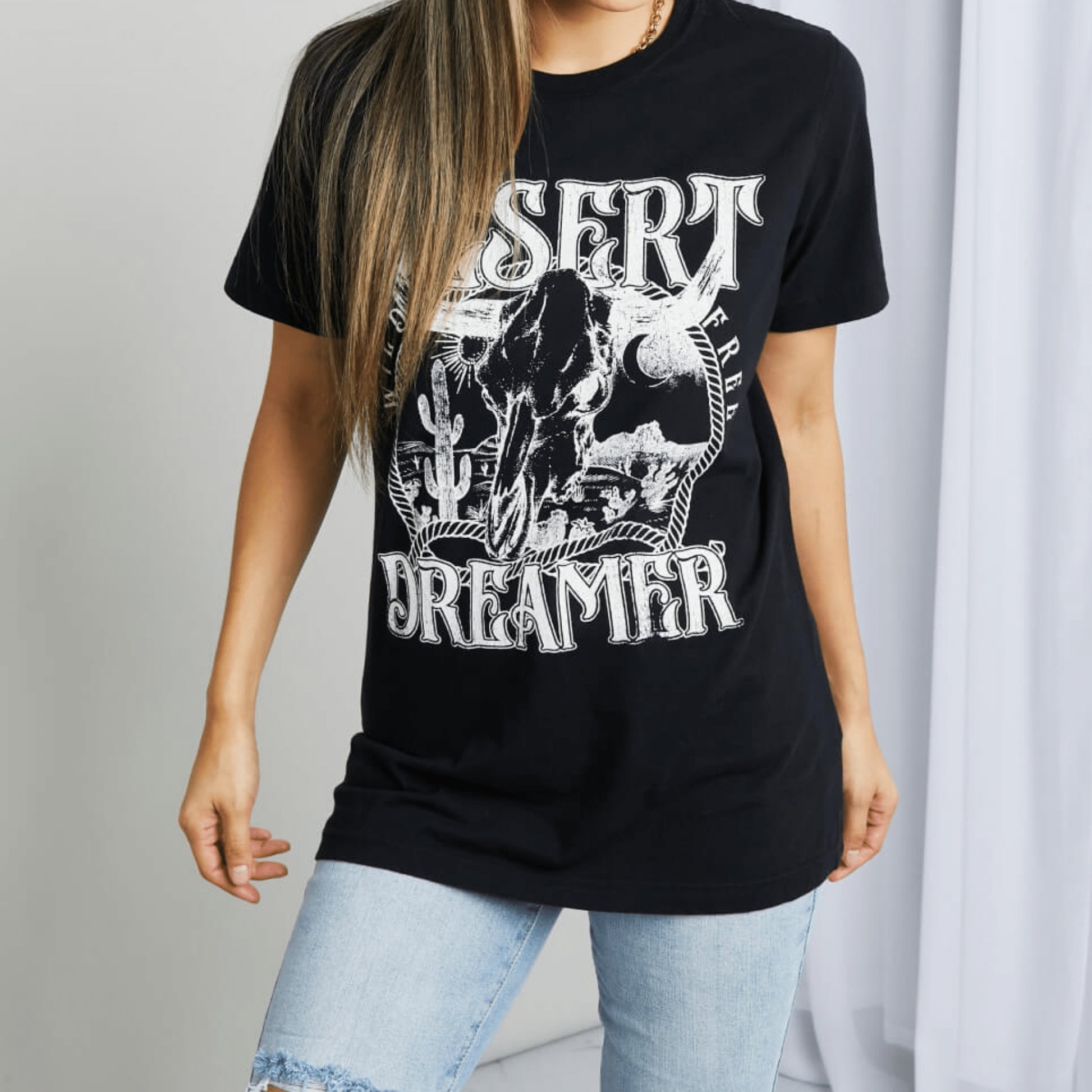 Frontal display of a woman wearing a black 'Desert Dreamer' tee with a beige hat.