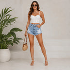 Full-body lifestyle photo of women's light wash distressed denim shorts styled with a white lace corset top and neutral summer accessories.