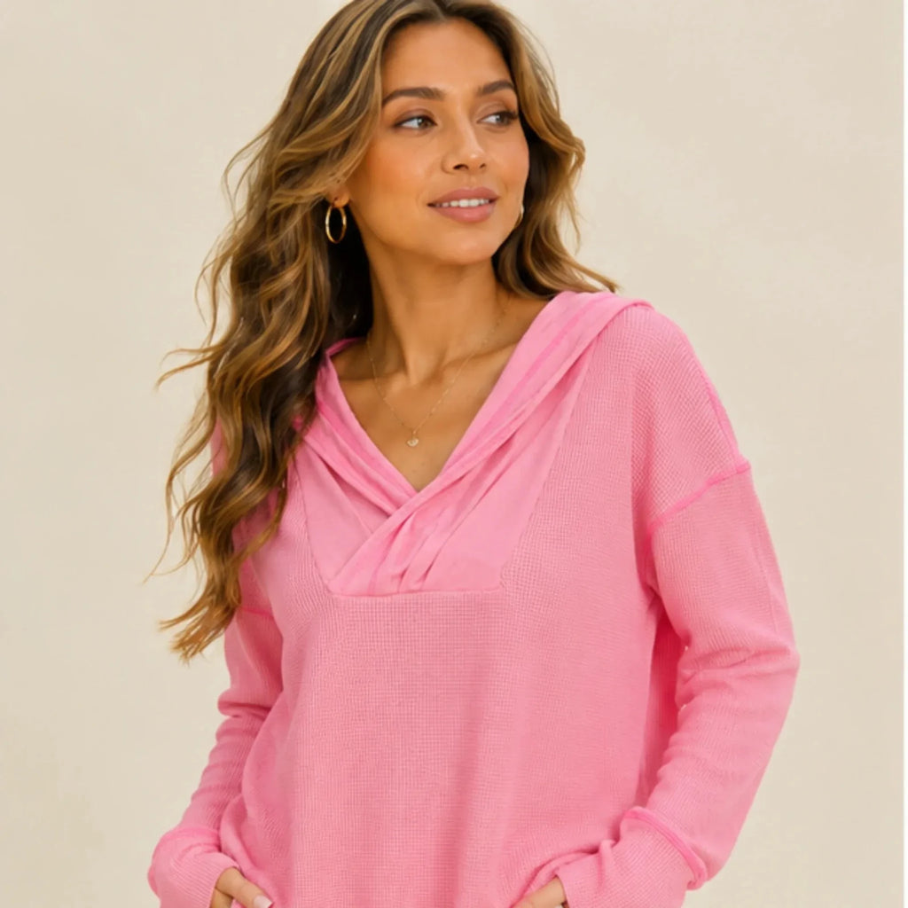 Women's pink drop shoulder waffle knit hoodie featuring a crossover hood, relaxed fit and long sleeves styled with white jeans.