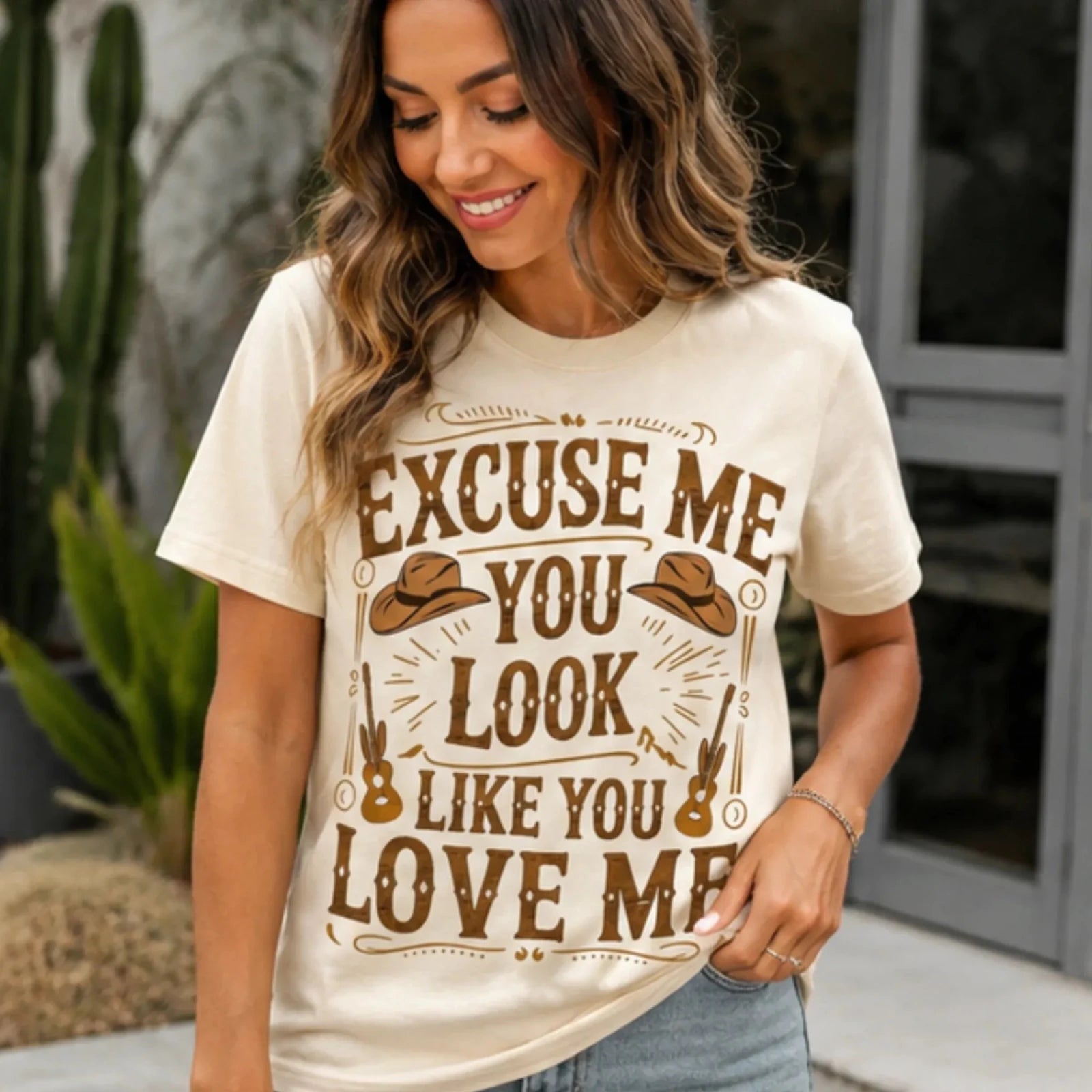 Woman wearing the natural "Excuse Me You Look Like You Love Me" western graphic tee styled with light wash jeans outdoors.