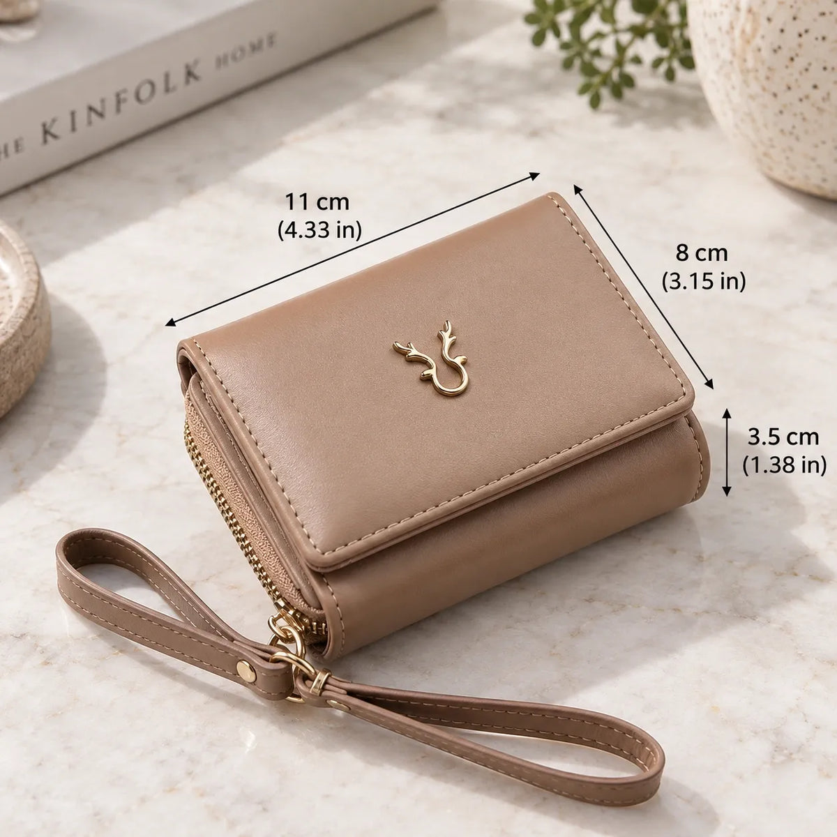 A beige wristlet wallet with a gold deer emblem and gold zipper, shown on a marble surface with dimension lines indicating its measurements: 11 cm (4.33 in) by 8 cm (3.