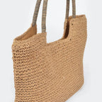 Angled view of a khaki faux straw tote bag with woven texture, spacious design, and striped shoulder handles.