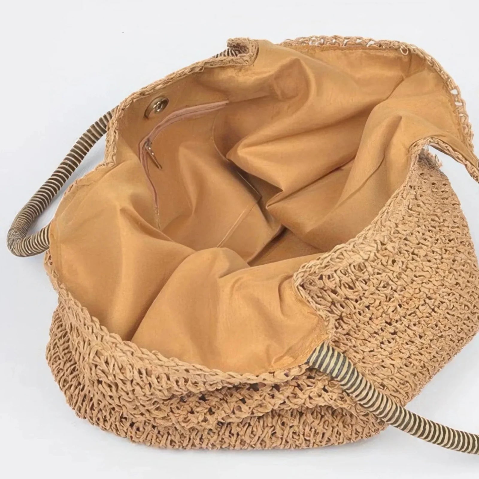 Interior of a khaki faux straw tote bag showing spacious fabric lining, zipper pocket, and magnetic snap closure.