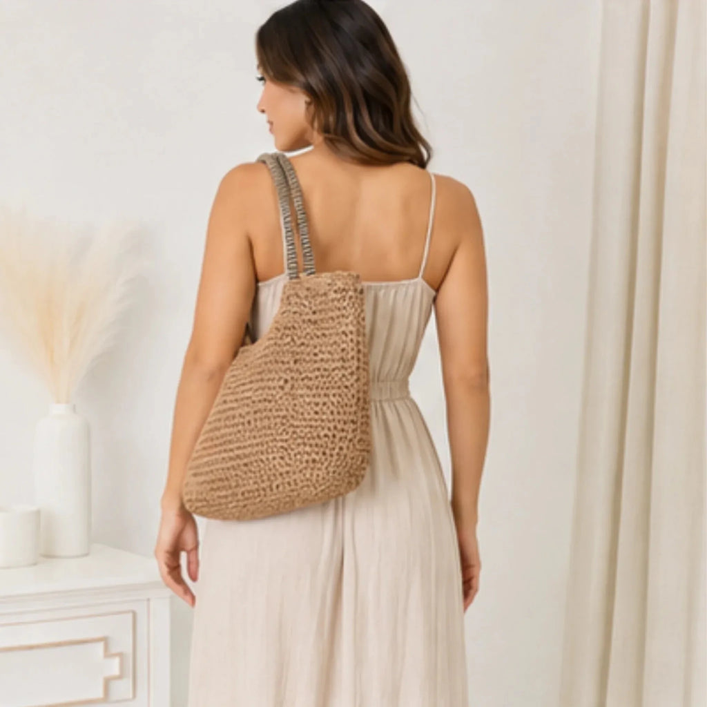 Back view of a woman wearing a khaki faux straw tote bag featuring woven texture and striped shoulder straps.