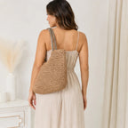 Back view of a woman wearing a khaki faux straw tote bag featuring woven texture and striped shoulder straps.