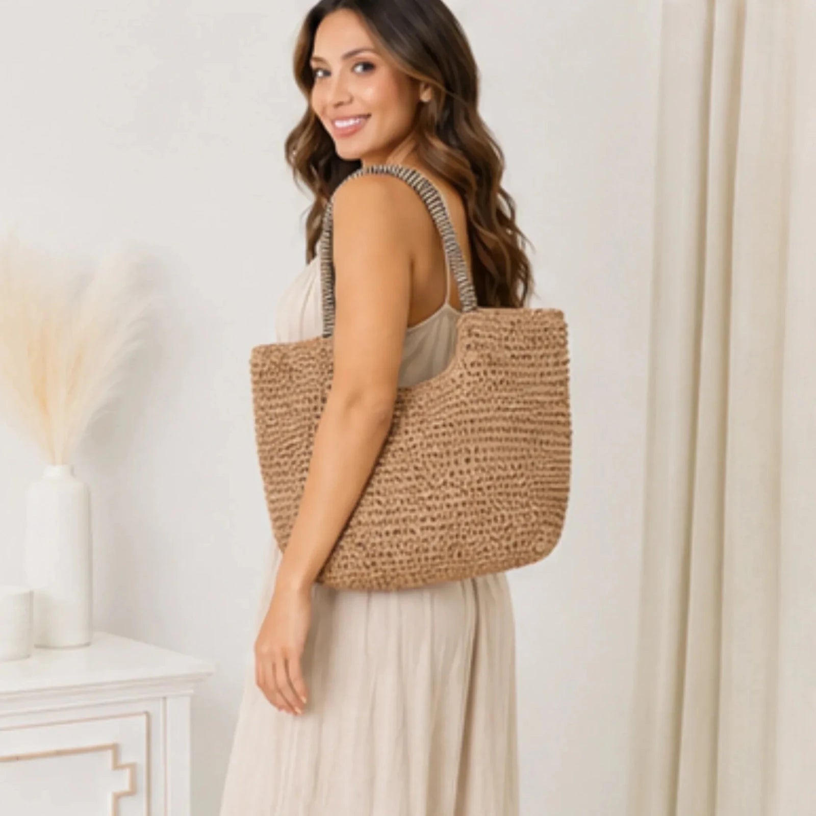 Side view of a woman carrying a khaki faux straw tote bag with woven design and striped shoulder handles.