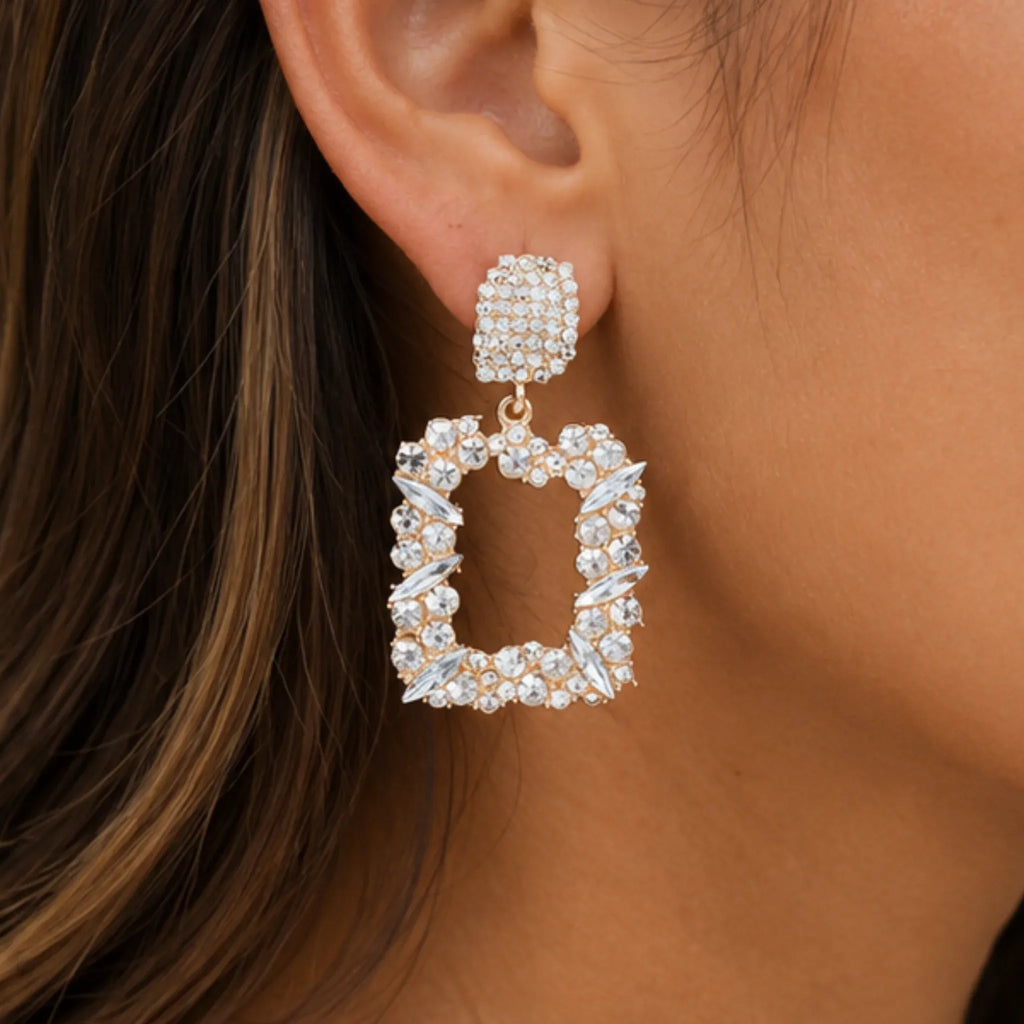 Close-up of gold rhinestone dangle earrings featuring sparkling crystal accents and geometric open-frame design.