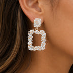 Close-up of gold rhinestone dangle earrings featuring sparkling crystal accents and geometric open-frame design.