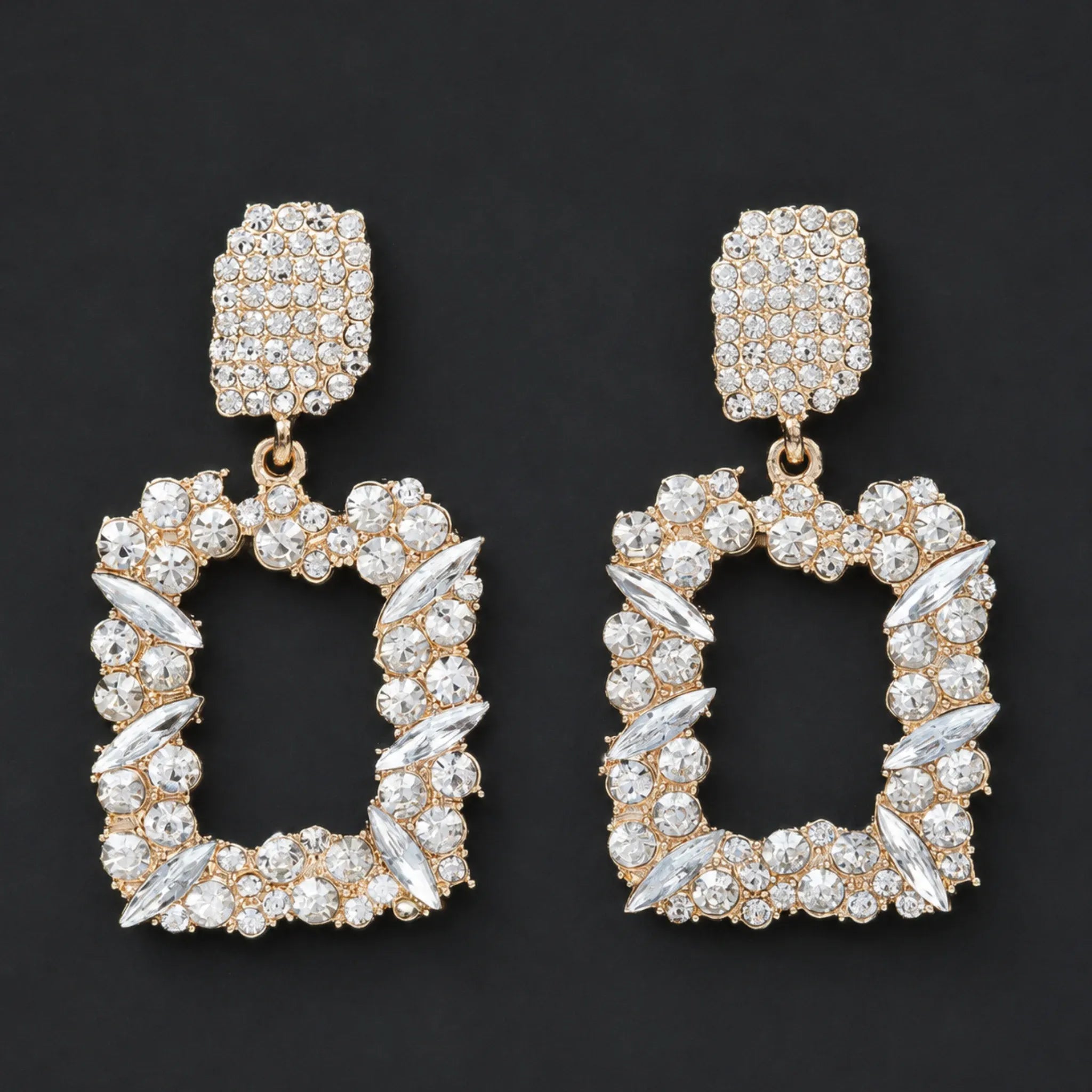 Gold rhinestone dangle earrings with sparkling crystal accents displayed in a flat lay on a black background.