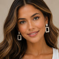 Woman wearing gold rhinestone dangle earrings shown from the front with sparkling geometric crystal details.