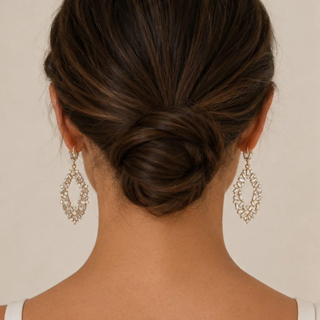 Back view of woman wearing gold rhinestone drop earrings with an elegant low bun hairstyle.