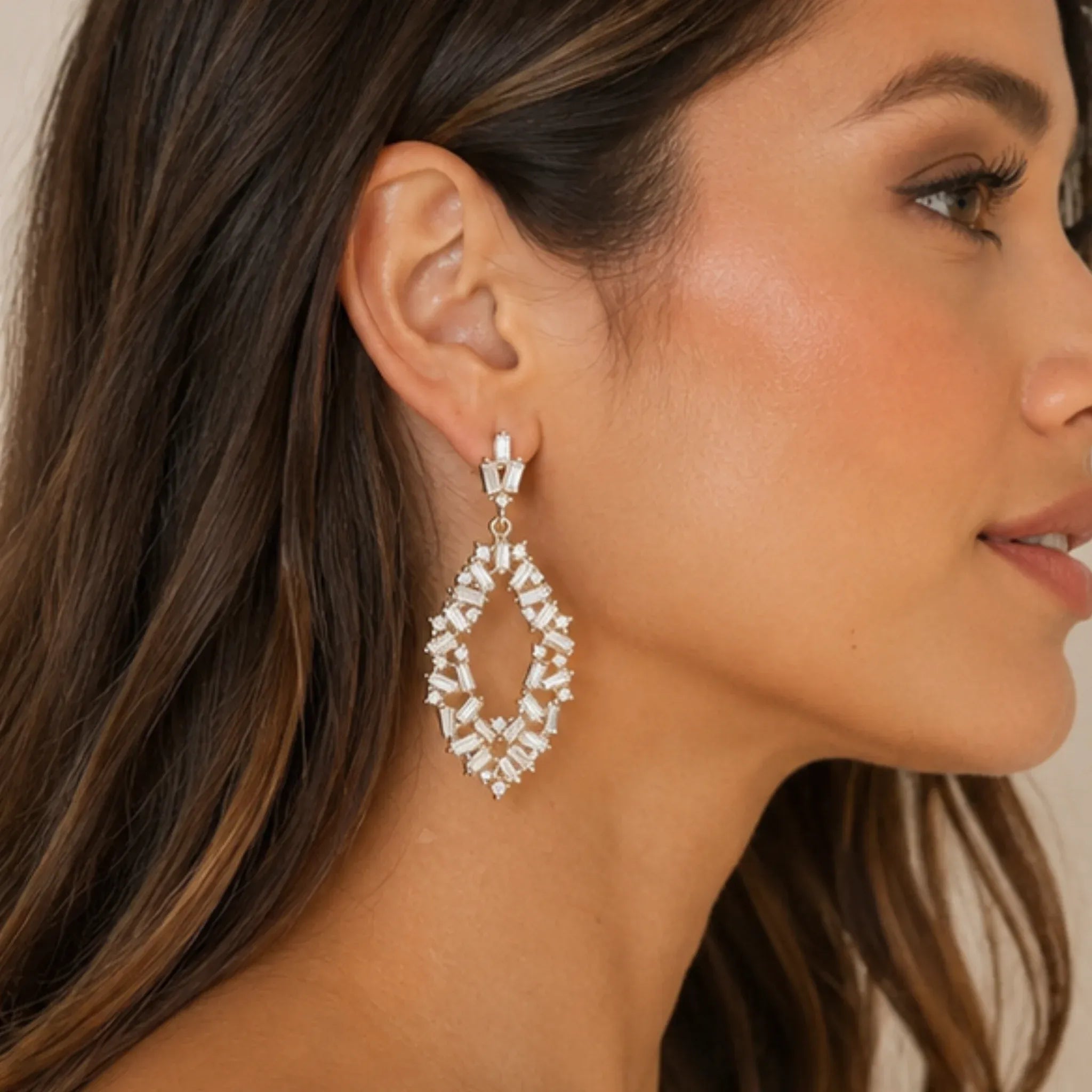 Side profile of woman wearing gold rhinestone drop earrings with elegant baguette-cut crystals.