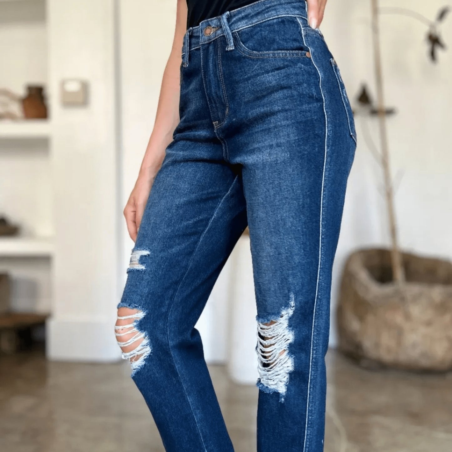 Side view of heavy destroy straight-leg jeans and white sneakers.