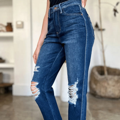Side view of heavy destroy straight-leg jeans and white sneakers.