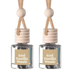 Two small clear glass reed diffusers with beige labels reading 'Iced Vanilla Woods,' beige ribbed stoppers, and natural wood beads on braided tan cords, shown on a white background.
