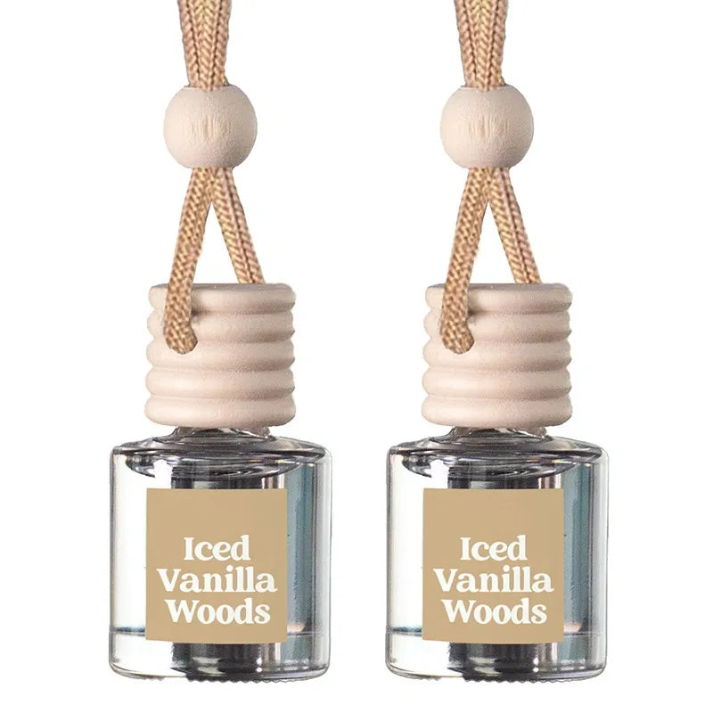 Two small clear glass reed diffusers with beige labels reading 'Iced Vanilla Woods,' beige ribbed stoppers, and natural wood beads on braided tan cords, shown on a white background.