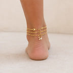 Back view of a layered gold initial anklet featuring three delicate chains with an adjustable extender and crystal accents.