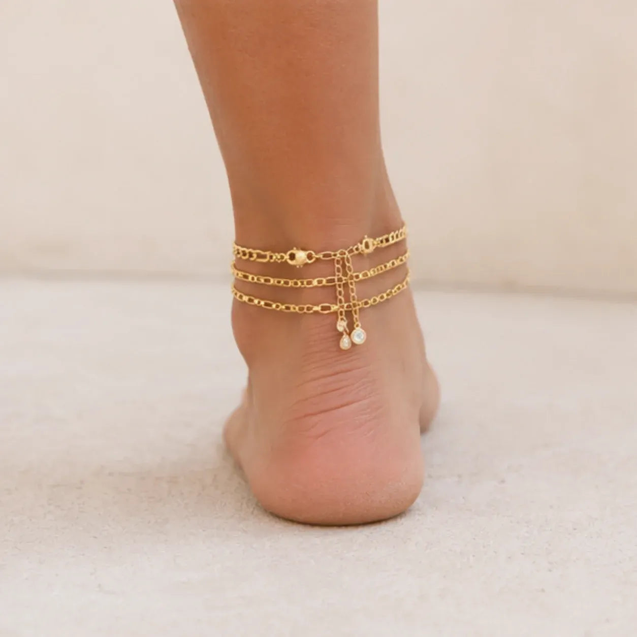 Back view of a layered gold initial anklet featuring three delicate chains with an adjustable extender and crystal accents.