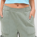 Close-up of sage green mineral wash wide leg cargo pants featuring the elastic waistband, soft fabric, and utility pocket detail.