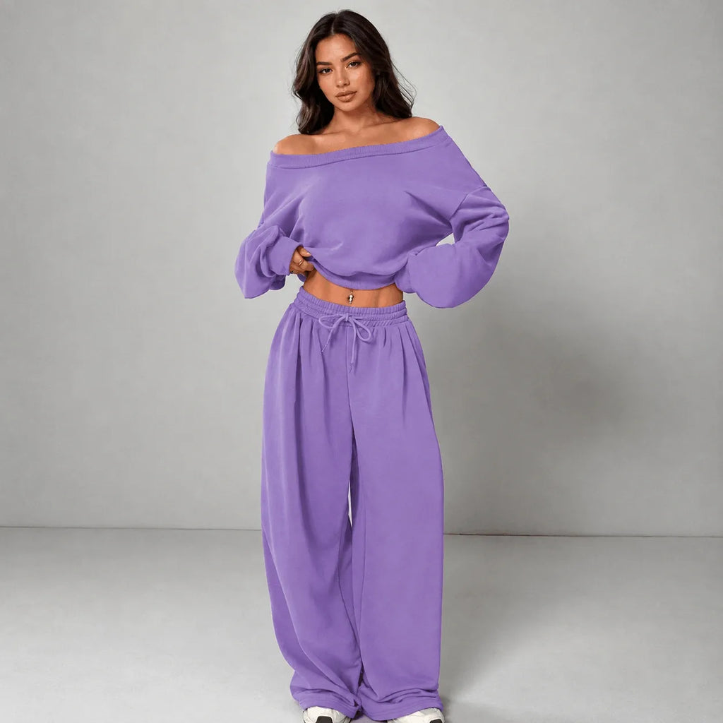 A woman modeling a matching lavender off-the-shoulder long-sleeve crop top and wide-leg drawstring sweatpants against a neutral gray studio background.