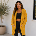 Woman wearing a yellow oversized cable knit open-front cardigan with hood and pockets
