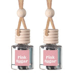 Two matching reed diffuser bottles with clear glass bodies, pink labels reading 'Pink Sugar,' beige reeds, and light wood beads on a white background.