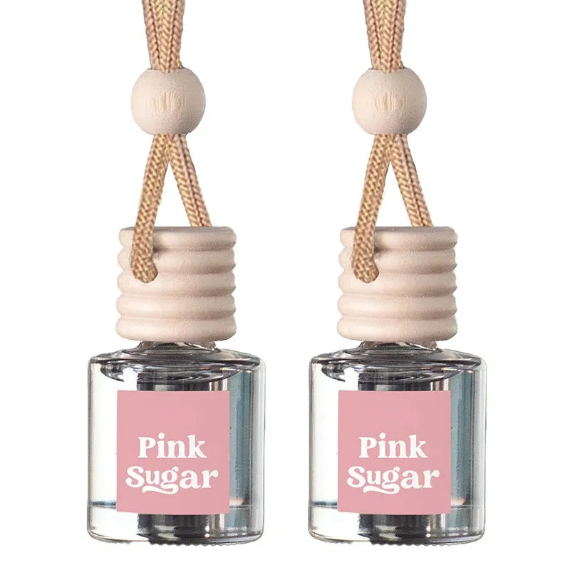 Two matching reed diffuser bottles with clear glass bodies, pink labels reading 'Pink Sugar,' beige reeds, and light wood beads on a white background.