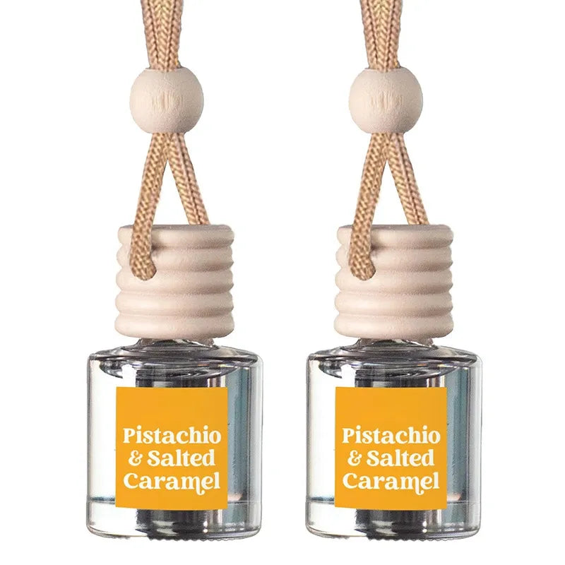 Two matching car air fresheners with clear glass bottles, beige wooden diffusers, and orange labels reading 'Pistachio & Salted Caramel', shown on a white background.