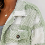 Close-up of soft sage green and white plaid plush fleece jacket fabric and button detail