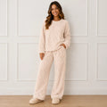 Woman wearing a cozy beige plush fleece pajama set with long sleeves, wide-leg pants, and bear detail