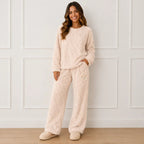 Woman wearing a cozy beige plush fleece pajama set with long sleeves, wide-leg pants, and bear detail
