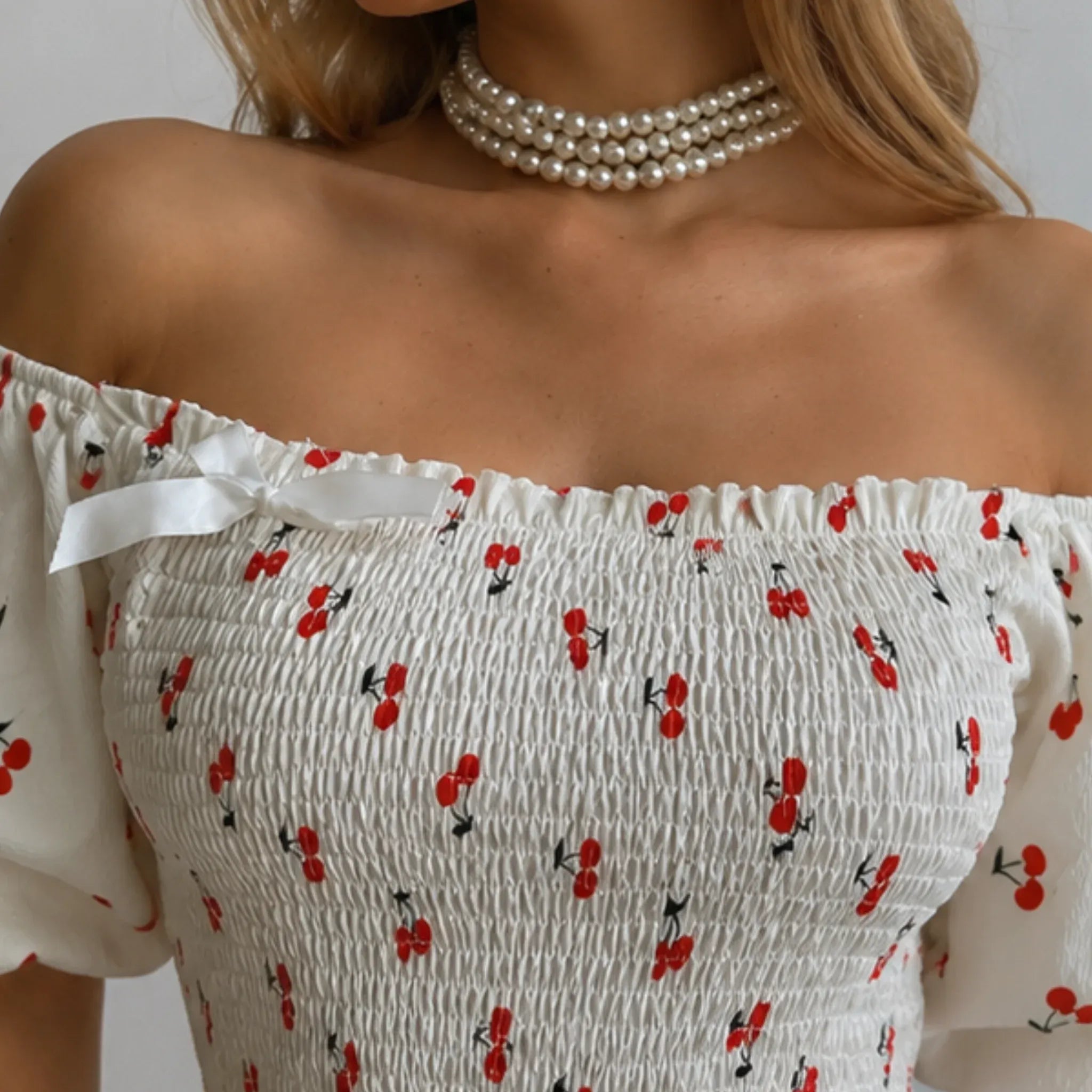 Women's Puff Sleeve Cherry Print Smocked Mini Dress close-up featuring an off-the-shoulder neckline, stretchy smocked bodice, white bow detail, and playful cherry print.