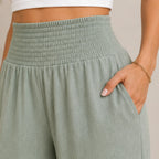 Close-up of sage lightweight high-waisted wide-leg lounge pants highlighting the smocked waistband, soft fabric, and side pocket.