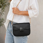 Close-up of a black faux leather shoulder bag highlighting the magnetic flap closure, smooth finish and gold chain strap.