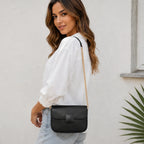 Side profile of a women's black faux leather shoulder bag with a gold chain shoulder strap and structured silhouette.