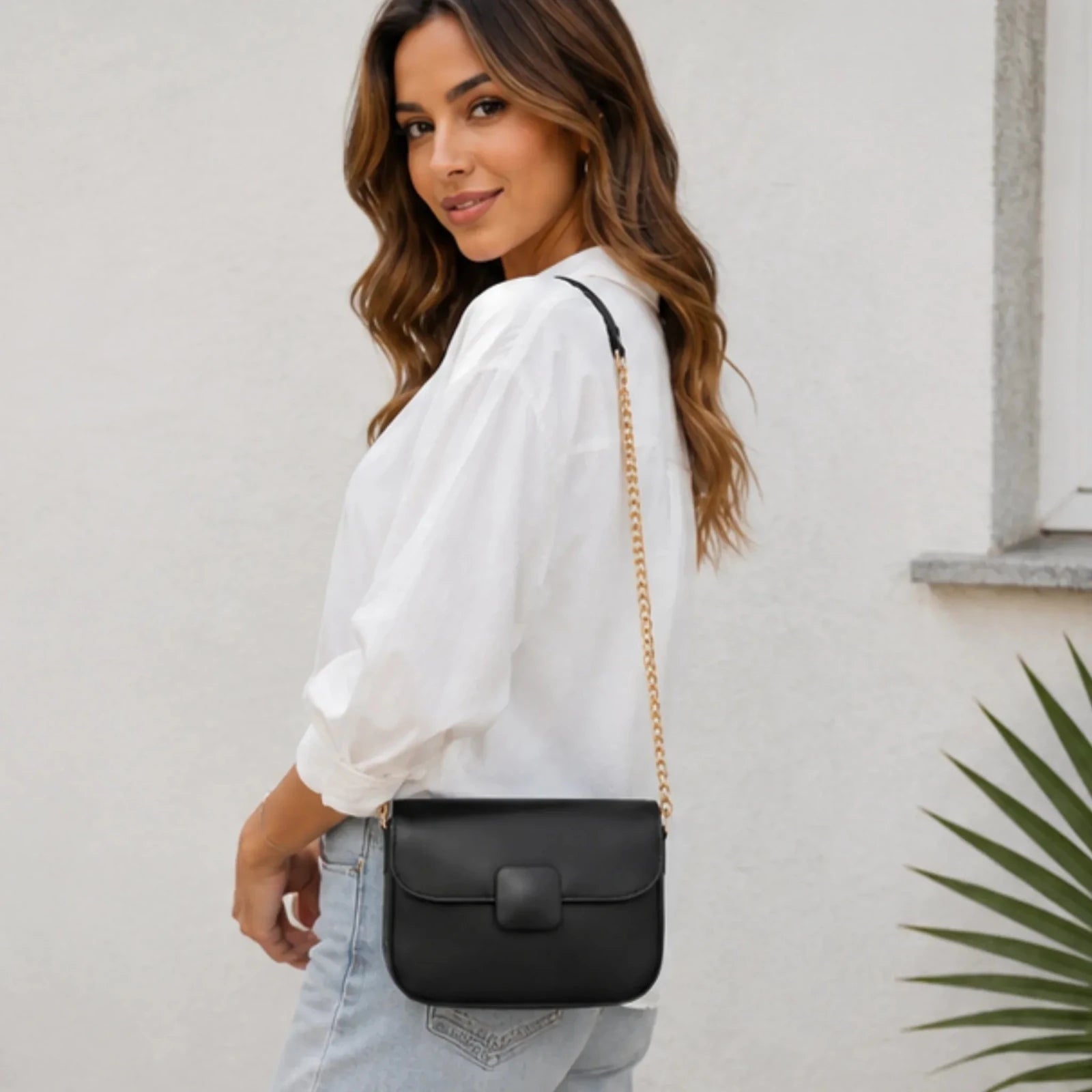 Side profile of a women's black faux leather shoulder bag with a gold chain shoulder strap and structured silhouette.