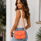 Women's coral faux leather shoulder bag with a structured silhouette and adjustable shoulder strap styled with casual denim.
